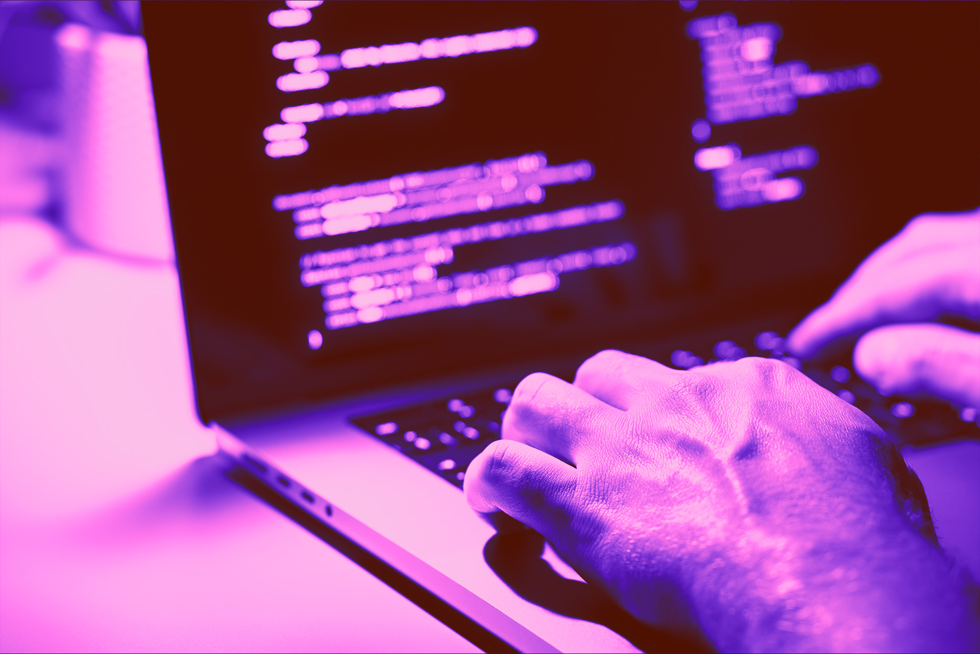 Hands typing on a laptop with code displayed on screen under purple lighting.